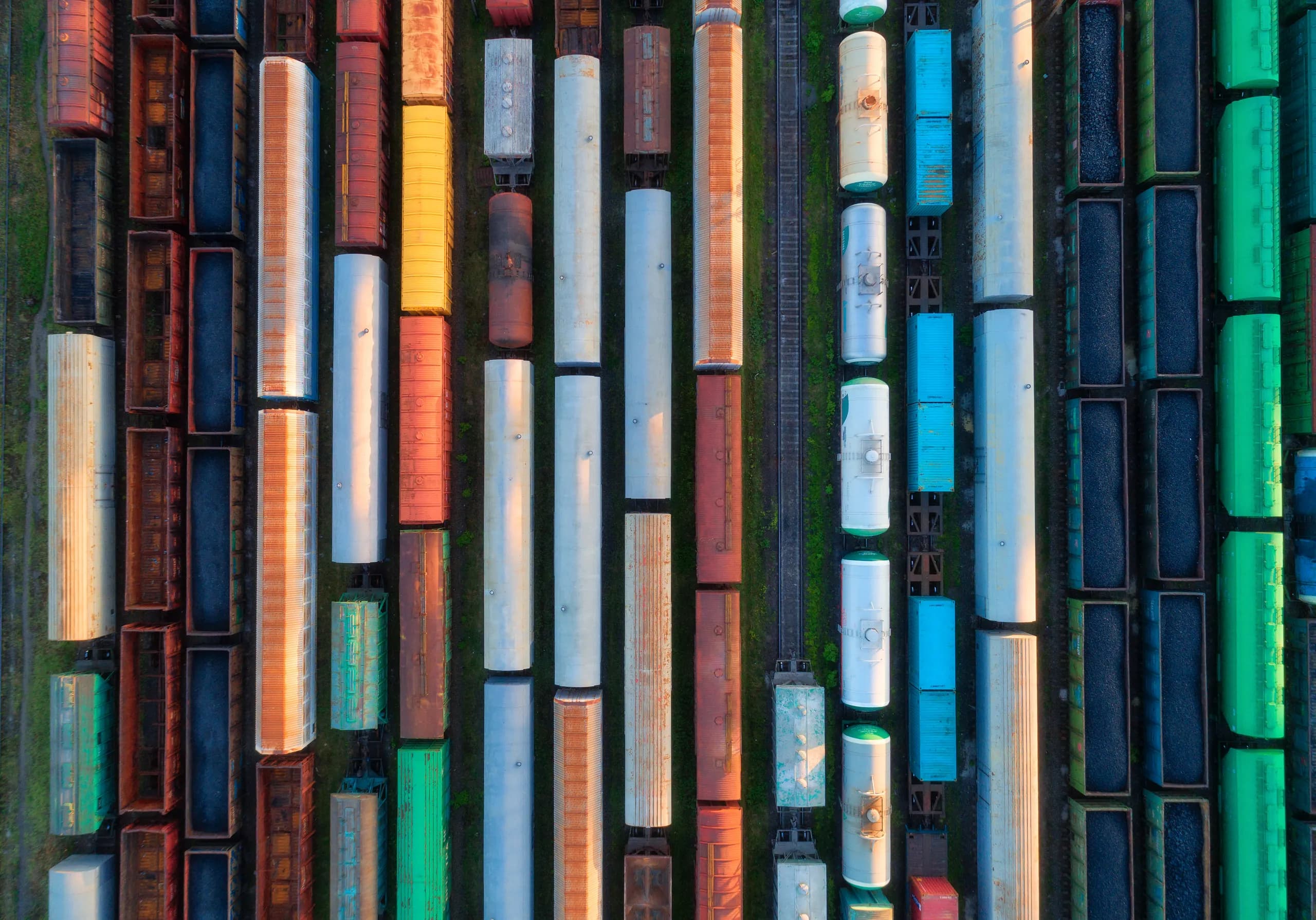 Aerial view of freight trains lined up in a rail yard at sunset — hoppers, tank cars, and containers in parallel rows