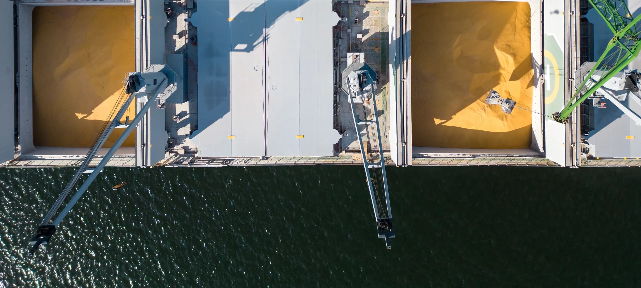 Aerial view of grain loading at port — bulk carrier holds, dockside crane, and open water